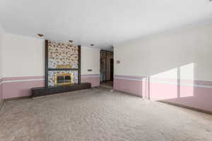 living room featuring a textured ceiling, ornamental molding, carpet flooring, and a stone fireplace