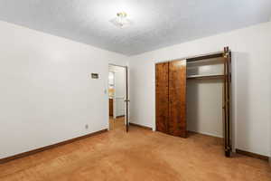 Unfurnished bedroom featuring light colored carpet, a closet, and a textured ceiling