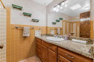 Bathroom with a shower, tile walls, tile patterned floors, and vanity