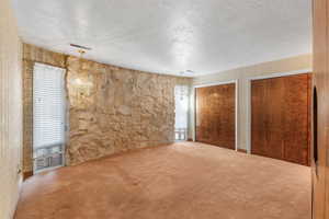 Primary bedroom with a textured ceiling, multiple closets, and carpet