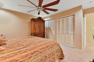 Primary bedroom with ceiling fan, carpet flooring, and two closets