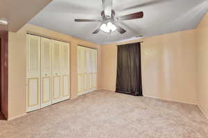 Bedroom with ceiling fan, light colored carpet, a textured ceiling, and two closets