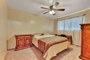 Carpeted bedroom with ceiling fan and a textured ceiling