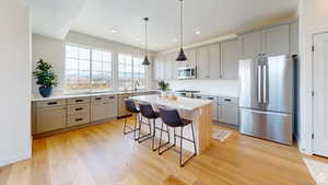 Kitchen featuring a kitchen island, decorative light fixtures, stainless steel appliances, a breakfast bar, and light hardwood / wood-style flooring