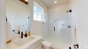 Bathroom featuring toilet, vanity, and a shower with shower door