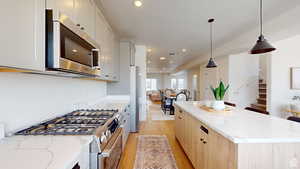 Kitchen featuring white cabinetry, light stone countertops, hanging light fixtures, and appliances with stainless steel finishes