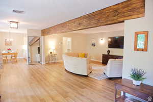 Living room with light hardwood / wood-style floors, beam ceiling, and a notable chandelier