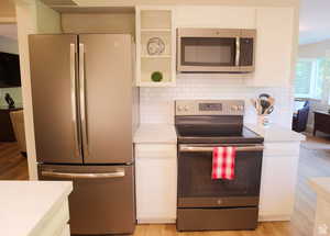 Kitchen featuring decorative backsplash, white cabinets, light hardwood / wood-style flooring, and stainless steel appliances