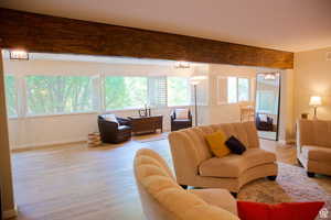 Living room with light hardwood / wood-style floors, a wealth of natural light, beam ceiling, and a chandelier