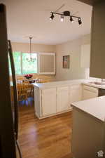 Kitchen featuring pendant lighting, kitchen peninsula, sink, light wood-type flooring, and white cabinets