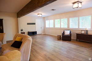 Living room featuring an inviting chandelier, beam ceiling, and wood-type flooring