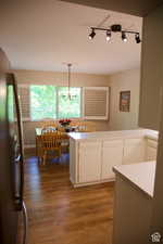 Kitchen featuring white cabinetry, hardwood / wood-style floors, kitchen peninsula, decorative light fixtures, and stainless steel refrigerator