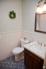 Bathroom featuring toilet, tile walls, tile patterned floors, and vanity