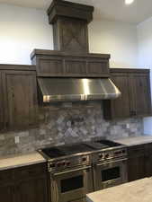 Kitchen featuring tasteful backsplash, double oven range, wall chimney range hood, and dark brown cabinets