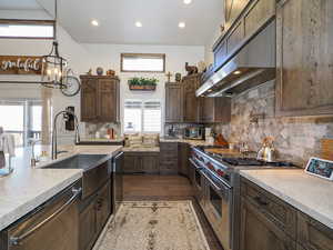 Kitchen with extractor fan, stainless steel appliances, pendant lighting, dark brown cabinetry, and sink