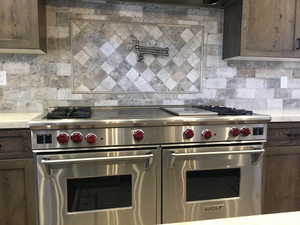 Kitchen featuring light countertops, range with two ovens, dark brown cabinets, and decorative backsplash