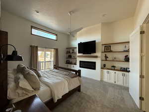 Carpeted bedroom featuring a textured ceiling, a high ceiling, a ceiling fan, access to exterior, and a glass covered fireplace