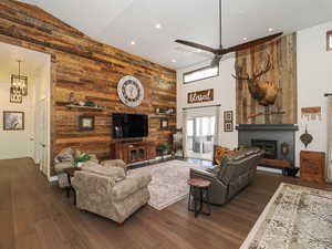 Living room with ceiling fan with notable chandelier, dark hardwood / wood-style flooring, lofted ceiling, and wooden walls