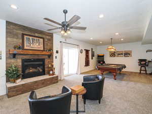 Carpeted living room featuring pool table, wood walls, and a stone fireplace