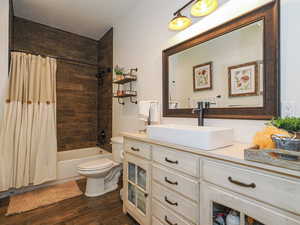 Full bathroom featuring toilet, hardwood / wood-style floors, shower / bathtub combination with curtain, a textured ceiling, and vanity