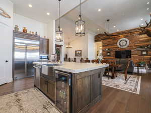 Kitchen featuring wood walls, a center island with sink, beverage cooler, built in fridge, and dark brown cabinetry