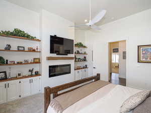 Carpeted bedroom featuring ceiling fan and a fireplace