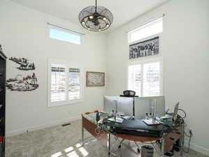 Carpeted office with a notable chandelier and a towering ceiling