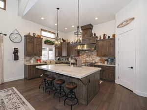 Kitchen featuring an island with sink, decorative backsplash, dark hardwood / wood-style floors, hanging light fixtures, and dark brown cabinetry