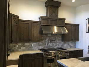 Kitchen featuring dark brown cabinetry, double oven range, light countertops, and decorative backsplash