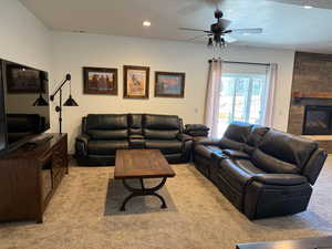 Living area with light colored carpet, a fireplace, a textured ceiling, and ceiling fan