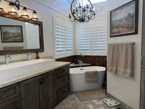 Full bathroom with a soaking tub, a wainscoted wall, vanity, wood walls, and a notable chandelier