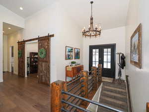 Foyer featuring a barn door, dark hardwood / wood-style flooring, lofted ceiling, french doors, and a chandelier