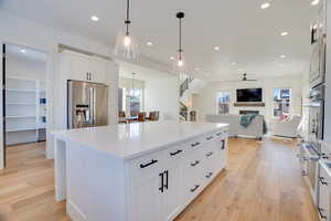 Kitchen with a spacious island, white cabinets, appliances with stainless steel finishes, hanging light fixtures, and ceiling fan