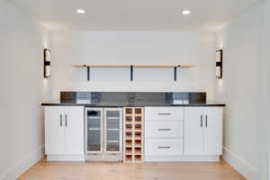 Bar featuring wine cooler, white cabinets, dark stone counters, and light hardwood / wood-style floors