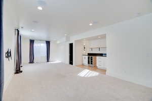 Unfurnished living room featuring bar and light colored carpet