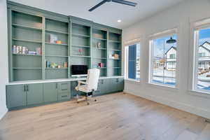 Unfurnished office featuring ceiling fan, built in desk, and light wood-type flooring