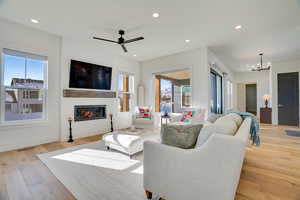 Living room with ceiling fan with notable chandelier and light hardwood / wood-style flooring