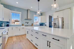 Kitchen with dishwashing machine, stainless steel fridge, wall chimney range hood, and white cabinetry