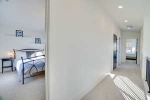 Hallway with lofted ceiling and light colored carpet