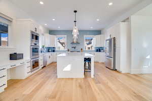 Kitchen with appliances with stainless steel finishes, light hardwood / wood-style floors, white cabinetry, and a kitchen island