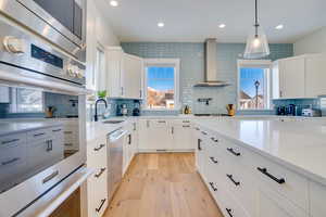 Kitchen with light stone countertops, white cabinets, wall chimney exhaust hood, sink, and backsplash