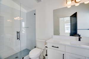 Bathroom featuring toilet, walk in shower, lofted ceiling, and vanity