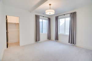 Unfurnished bedroom featuring a spacious closet, light colored carpet, a closet, and beam ceiling