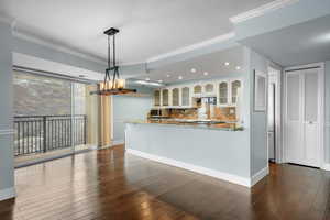 Kitchen featuring decorative backsplash, dark wood-type flooring, light stone countertops, crown molding, and white cabinets