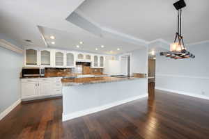 Kitchen with white fridge, backsplash, hanging light fixtures, dark stone counters, and white cabinets