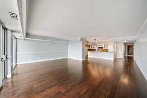 Unfurnished living room featuring dark hardwood / wood-style floors, crown molding, and an inviting chandelier