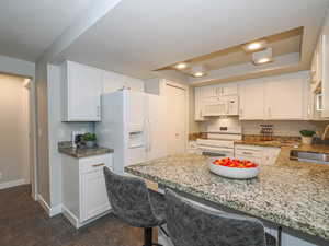 Kitchen with white cabinets, a breakfast bar, and white appliances