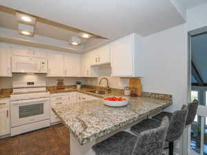 Kitchen with a breakfast bar, kitchen peninsula, sink, white appliances, and white cabinetry