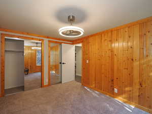 Unfurnished bedroom featuring carpet, wood walls, and two closets