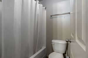 Bathroom featuring toilet and shower / tub combo with curtain